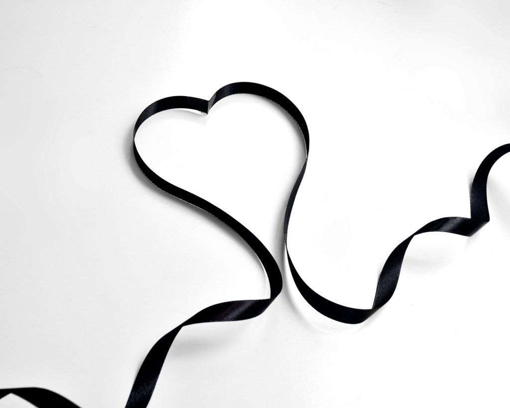 From above of long black decorative ribbon in shape of heart placed on white background in modern light art studio